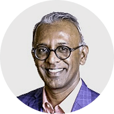 Dr. Manjunath Vadmal, smiling, in round glasses and a blue checked jacket